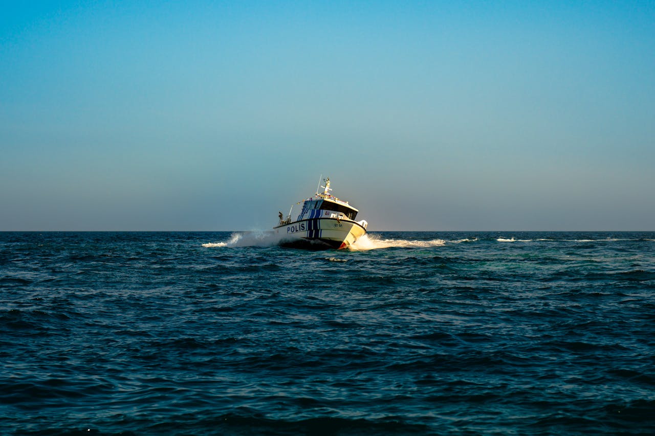 A police boat speeds across the open sea under a clear blue sky.